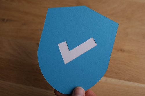 Closeup shot of a man holding a blue protection shield icon with a white checkmark on it